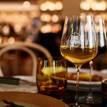A glass of white wine on the table showing the Bar Vino logo frosted on the outside of the glass.